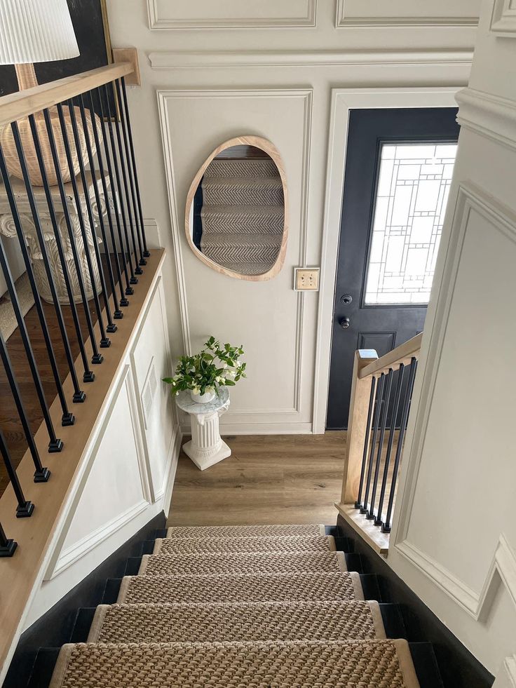 the stairs are made of wood and have black handrails, with a round mirror above them