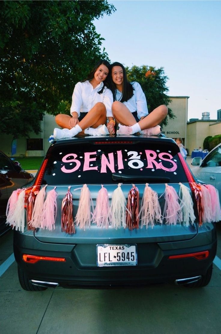 two women sitting on the back of a car decorated with pink and white tassels