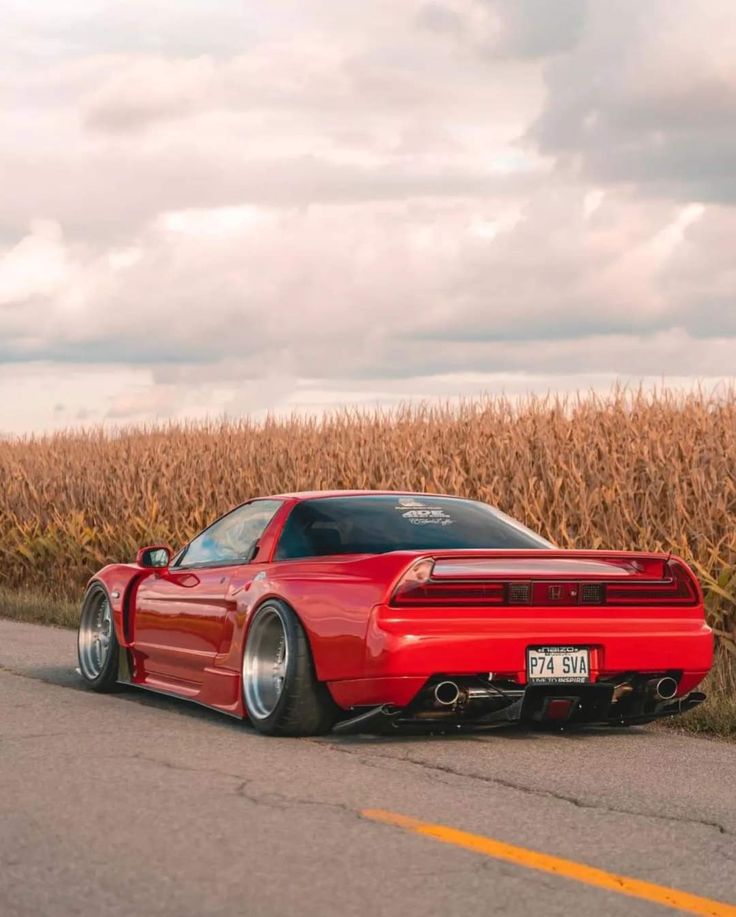 a red sports car is parked on the side of the road in front of a cornfield