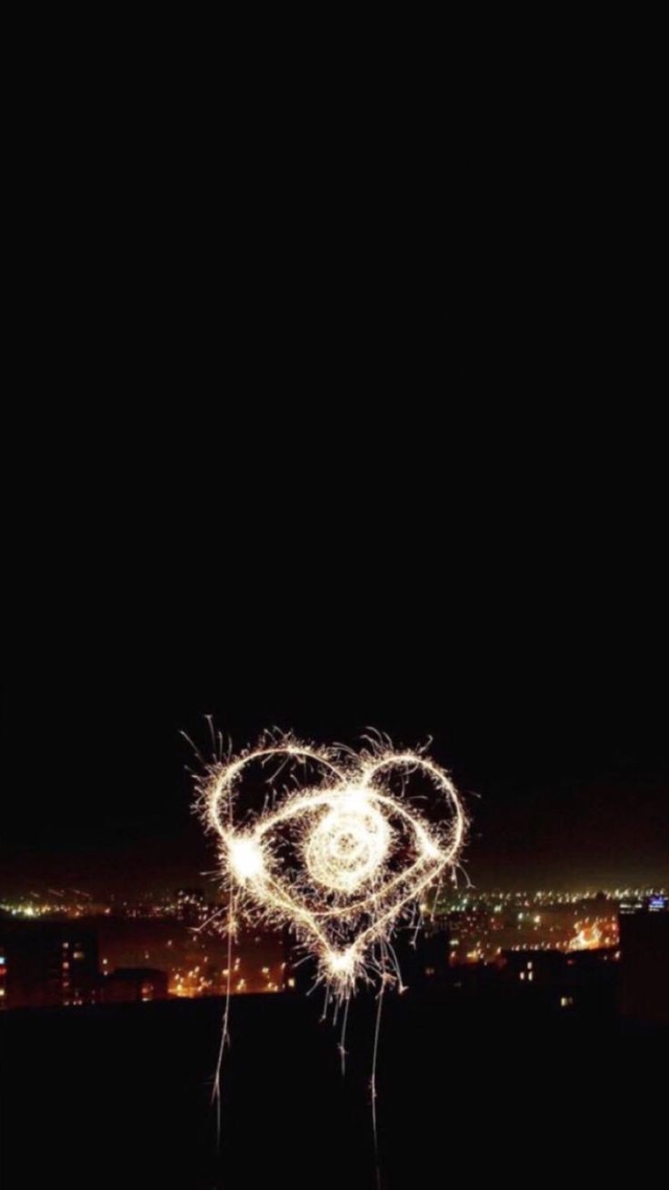 fireworks in the shape of a heart on top of a hill with city lights behind it