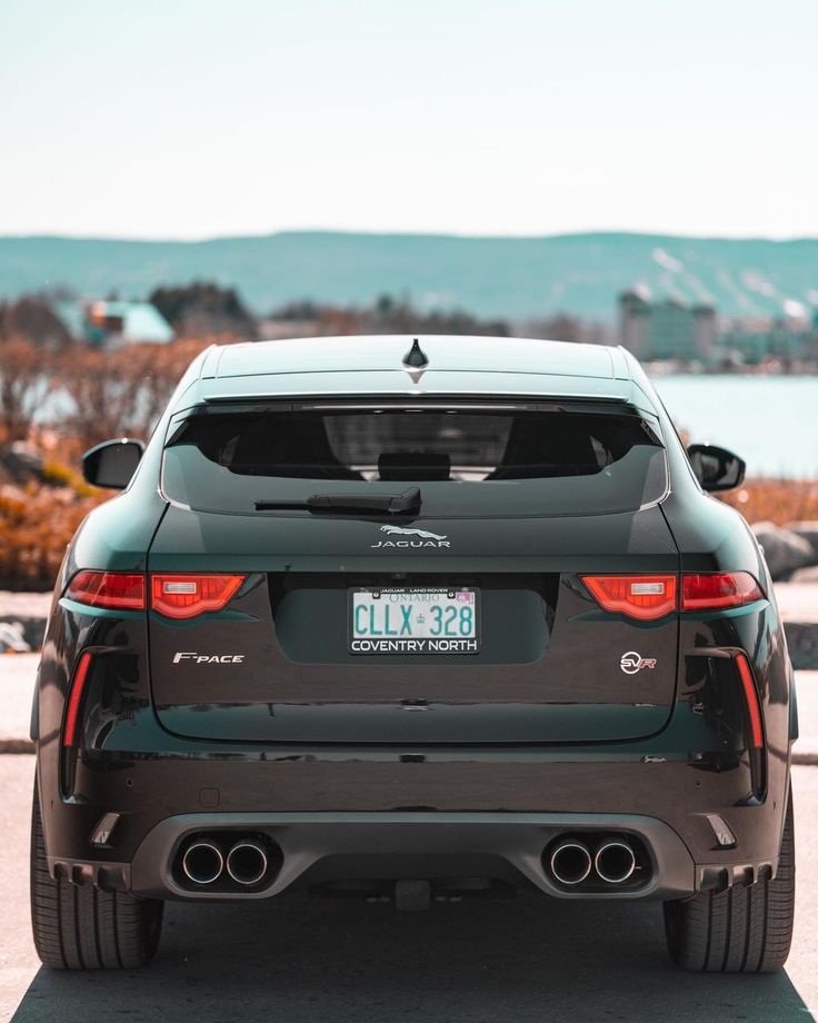 the back end of a black car parked in a parking lot next to some water