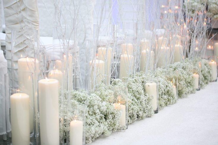 candles are lined up along the wall with white flowers and greenery on each side