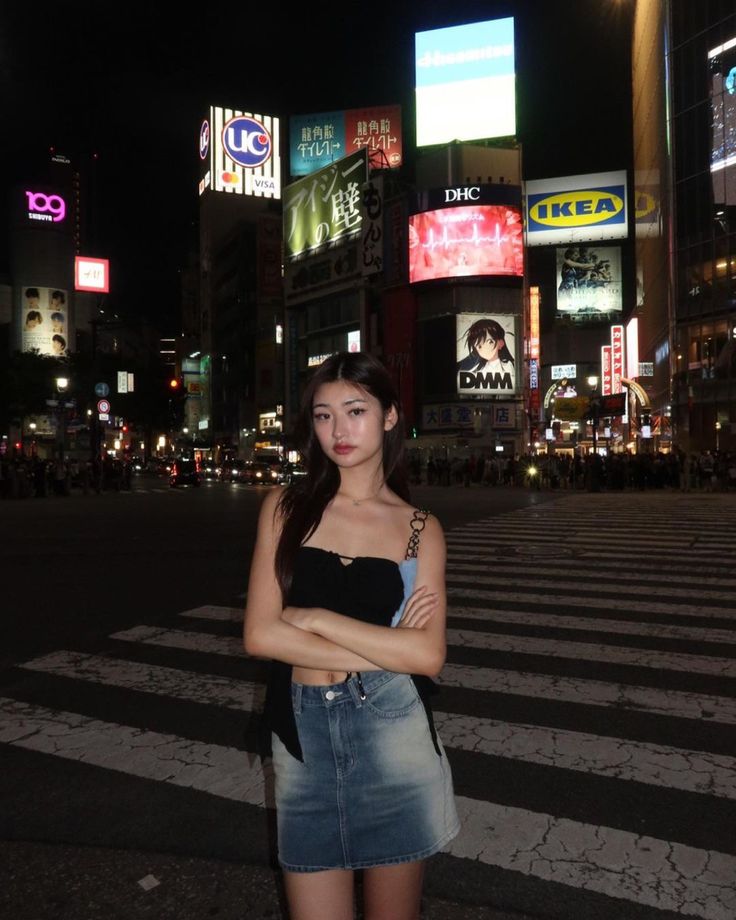 a woman standing in the middle of a cross walk at night with her arms crossed