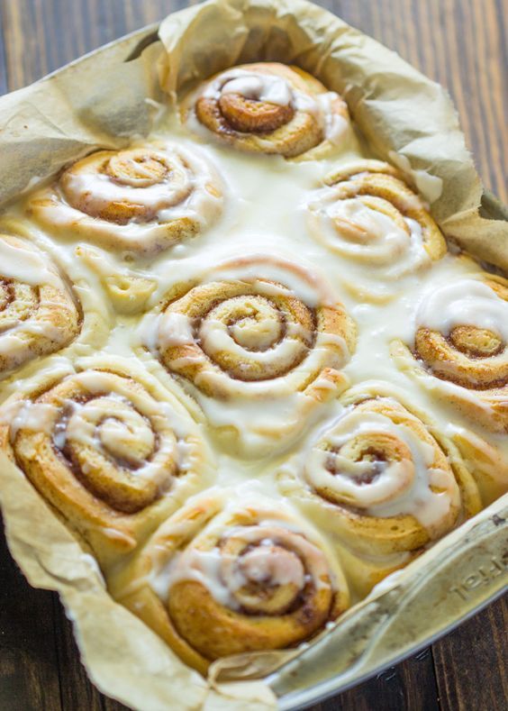 cinnamon rolls in a baking pan next to a cup of milk on a wooden table