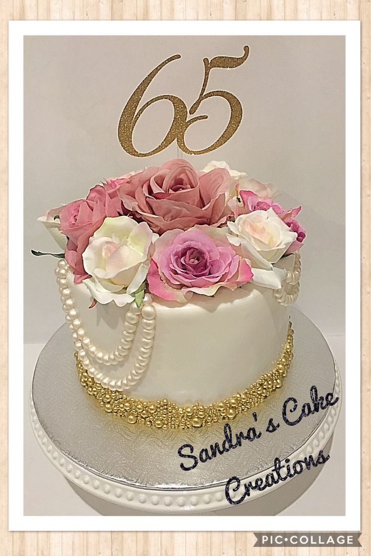 a white cake with pink flowers and pearls on the top is decorated with gold lettering