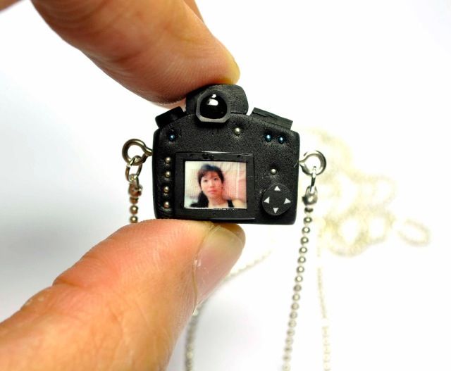 a hand holding a tiny camera with a photo attached to it