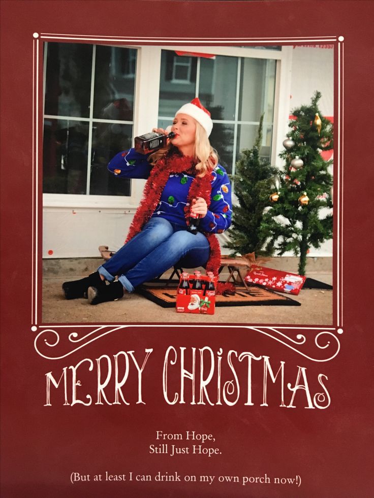 a woman sitting on the ground drinking from a bottle in front of a christmas tree