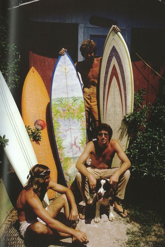 three men sitting on the ground with surfboards behind them