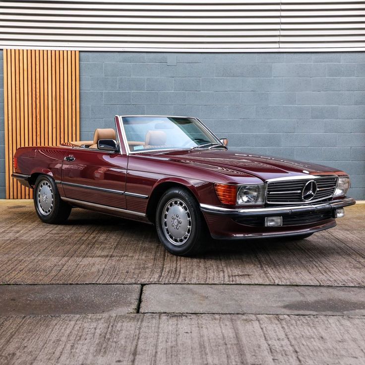 a red mercedes benz convertible parked in front of a building with graffiti on the wall