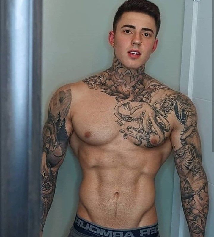 a man with tattoos on his chest standing in front of a mirror wearing trunks and looking at the camera