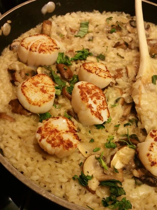 scallops and mushrooms are being cooked on top of rice in a skillet