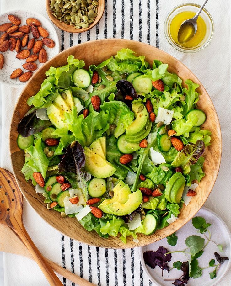 a salad in a wooden bowl on top of a striped table cloth next to nuts