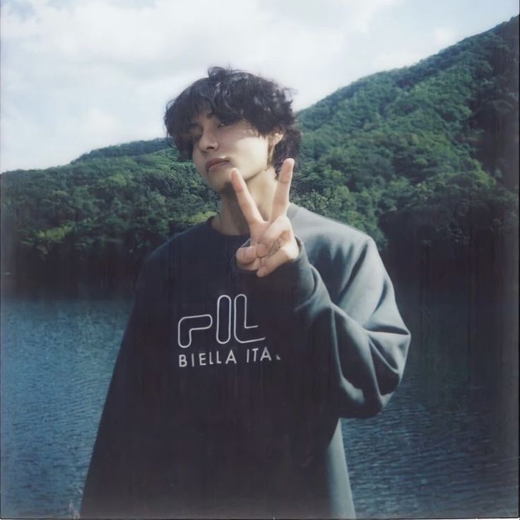 a young man making the peace sign with his hand while standing in front of a lake