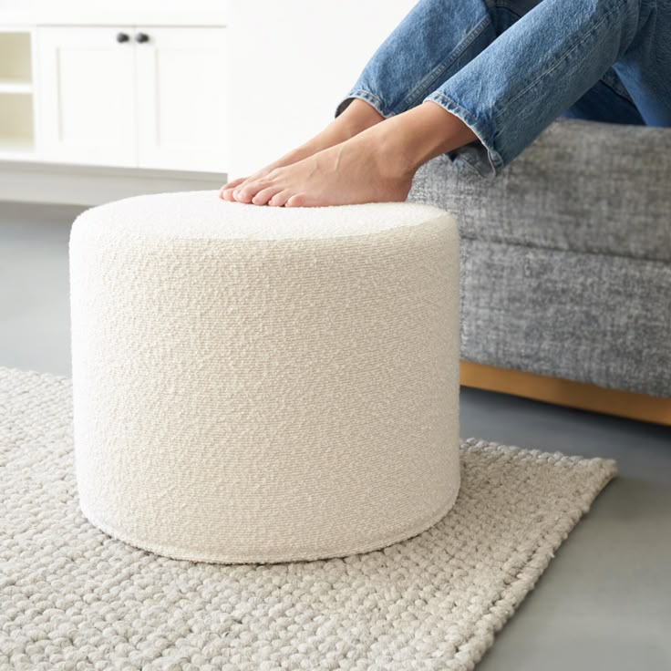 a person sitting on top of a white ottoman with their feet resting on the ottoman