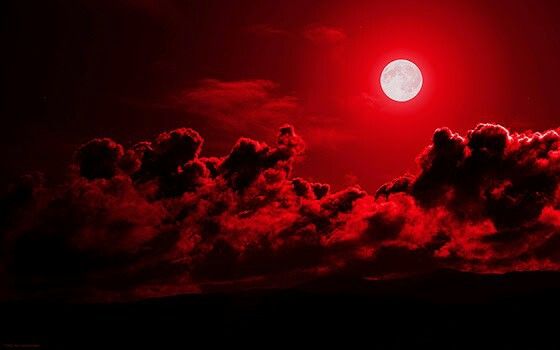 the full moon is shining red in the night sky with clouds and mountains below it