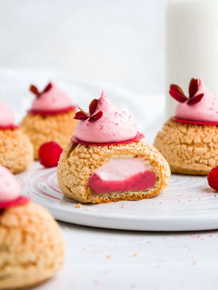 small pastries with pink icing and raspberries on a plate