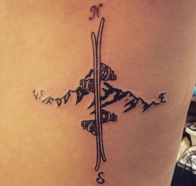 a snowboard tattoo on the back of a woman's thigh, with mountains in the background