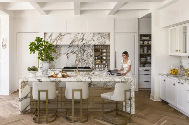 a woman sitting at a kitchen island in front of a marble counter top and white chairs