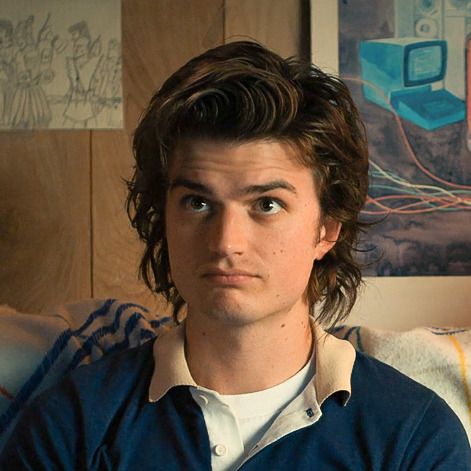 a young man sitting on top of a couch in front of a wall covered with pictures