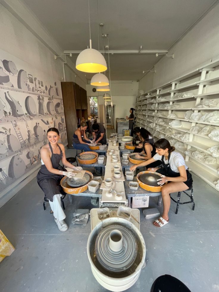 a group of people working on pottery in a room filled with shelves and shelving