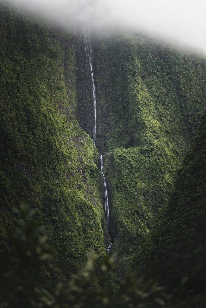 a tall waterfall surrounded by lush green hills