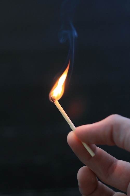 a hand holding a lit matchstick in the dark