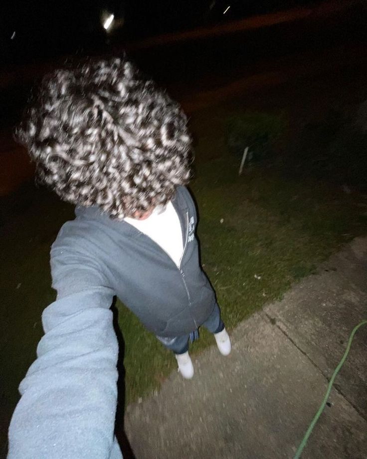 a young boy is walking down the sidewalk at night with his skateboard in hand