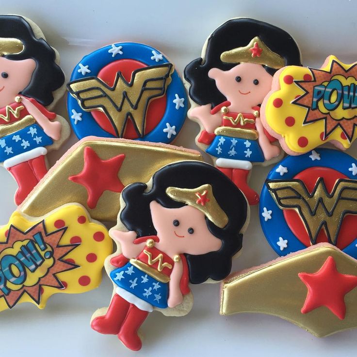 some decorated cookies are laying on a white tablecloth and have wonder woman emblems on them