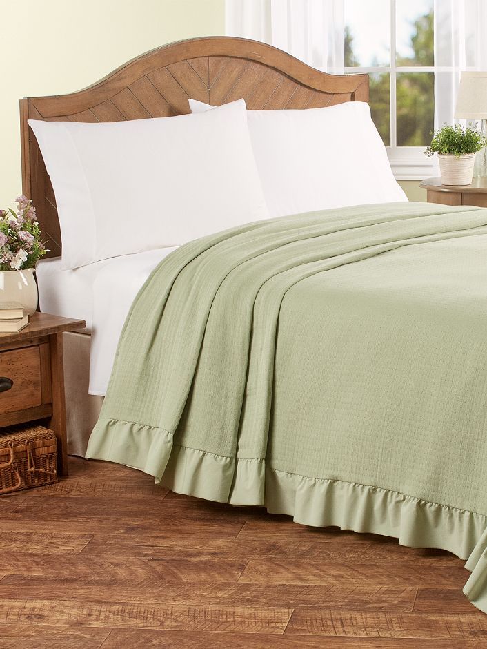 a bed with white sheets and green bedspread next to a wooden headboard