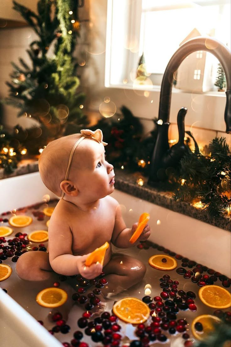 a baby sitting in a bathtub with orange slices and cranberries on the floor