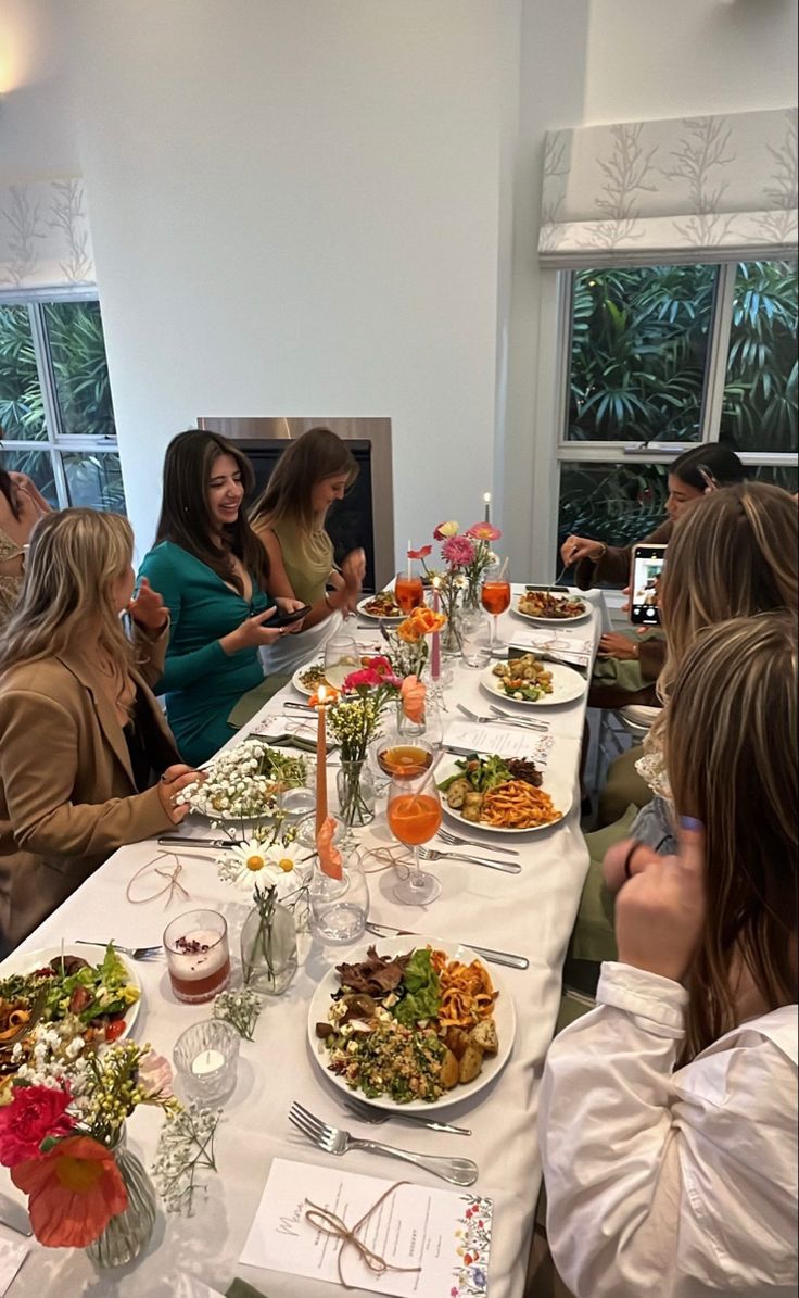 a group of women sitting at a long table with plates of food and drinks on it