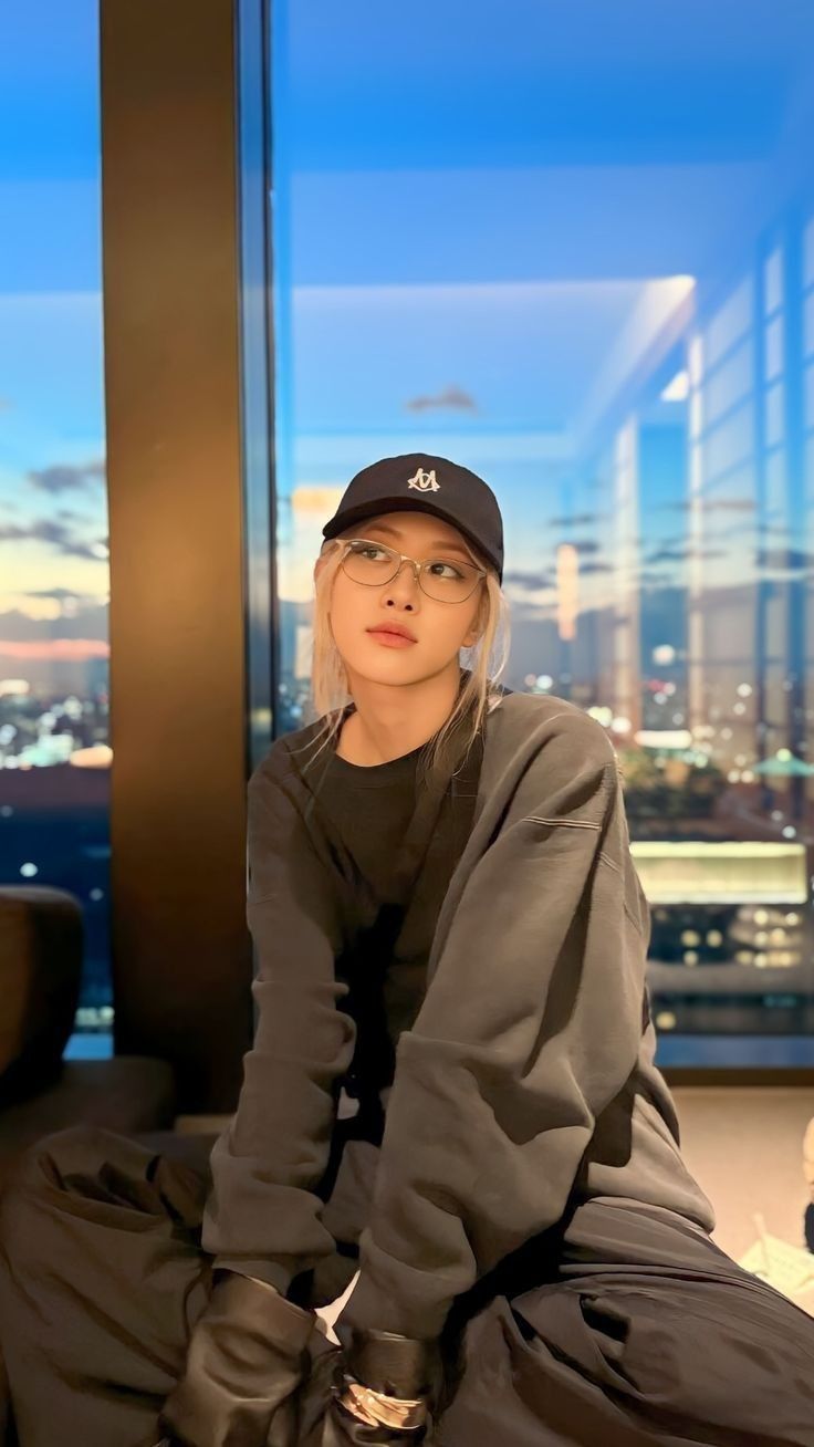 a woman sitting on top of a bed in front of a window wearing a hat