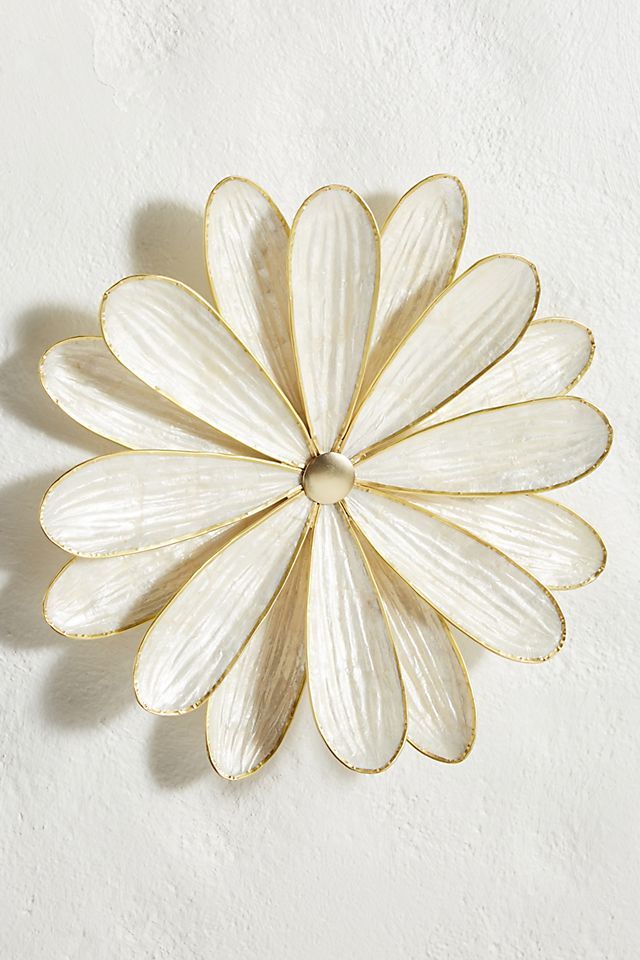 a white and gold flower shaped wall decoration on a white wall with a shadow from the petals