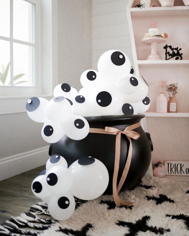 black and white balloons are sitting in a pot on the floor next to a shelf