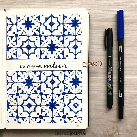 an open notebook with blue and white designs on it next to two black pens,