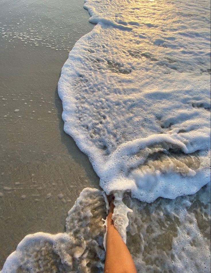 a person standing on top of a sandy beach next to the ocean with waves coming in