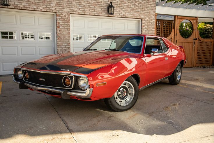 an orange and black muscle car parked in front of a brick building with two garage doors