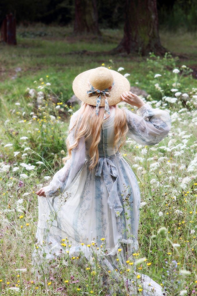 a woman in a dress and hat walking through a field with wildflowers on the ground