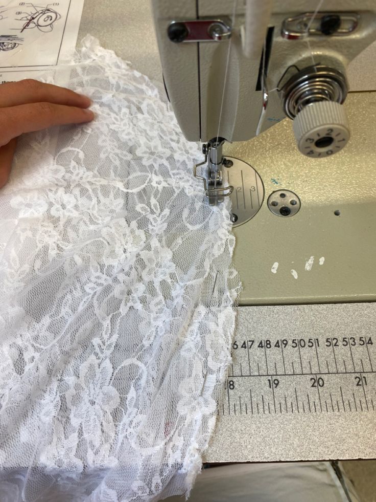 someone using a sewing machine to sew lace on a piece of white fabric with a measuring tape