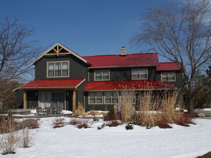 a large house with a red roof in the middle of some snow covered grass and trees