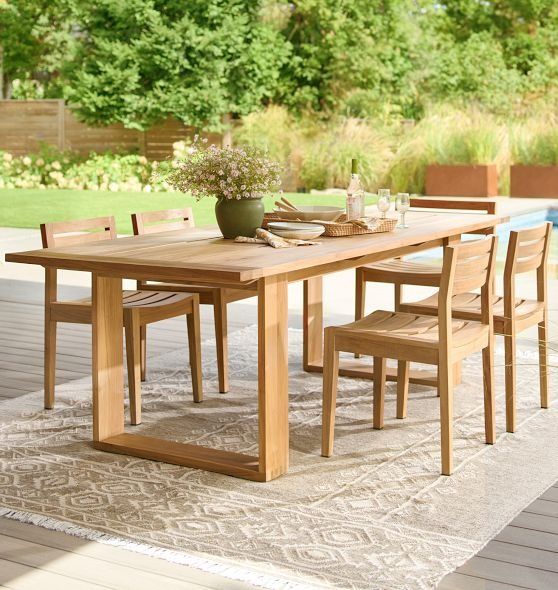 a wooden table and chairs sitting on top of a rug next to a swimming pool