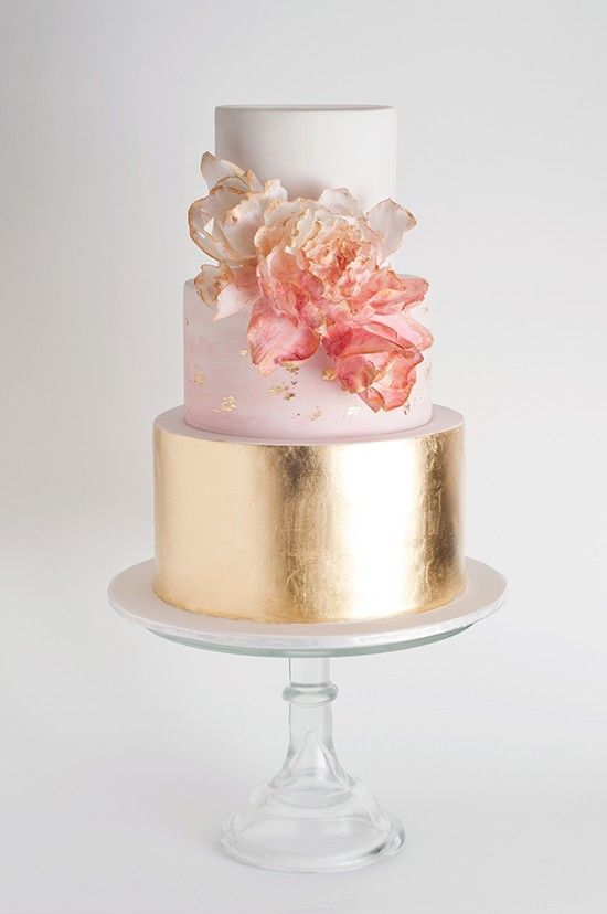 a three tiered cake with pink and gold flowers on the top is sitting on a glass stand