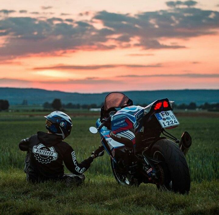 two motorcyclists sitting in the grass watching the sun go down on their bikes