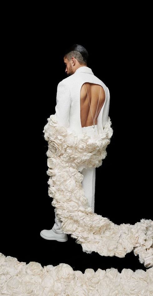 a man in a white suit standing on top of a pile of flowers with his back to the camera