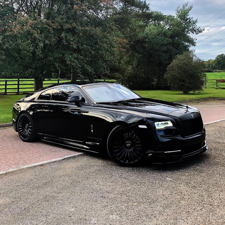 a black car parked on the side of a road next to a lush green field