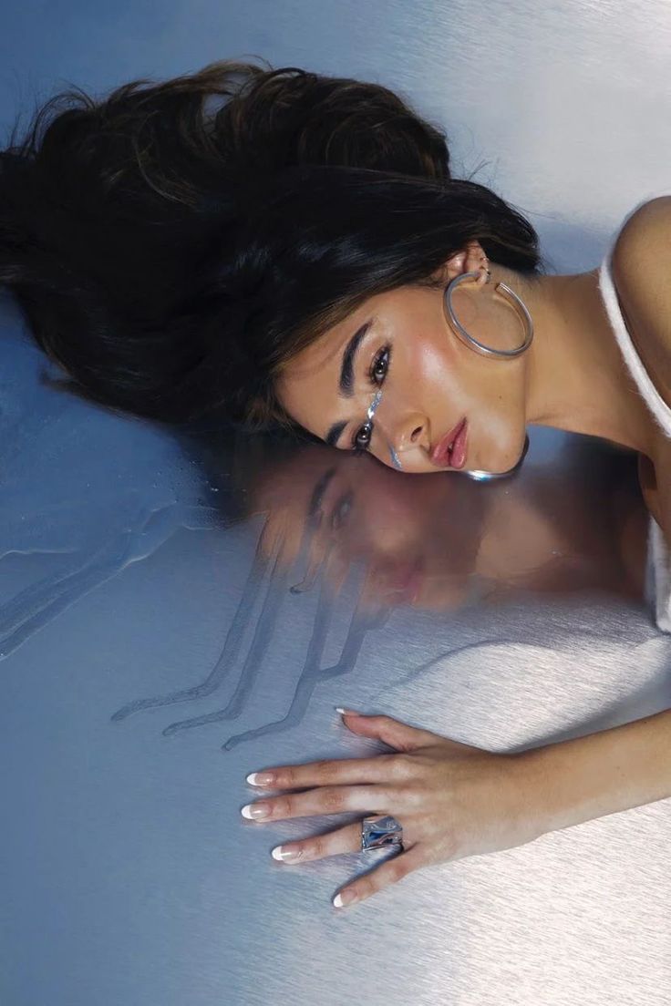 a beautiful woman laying on top of a bed next to her hand and nail polish