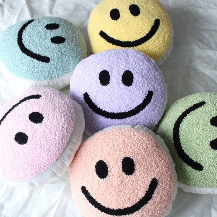 four different colored smiley face pillows sitting on top of a white sheet with black dots