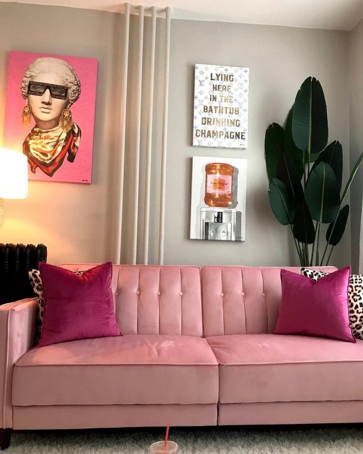 a living room with pink couches and pictures on the wall above them, along with a large potted plant