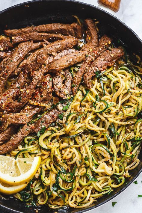 steak and noodles in a skillet with lemon wedges on the side for garnish