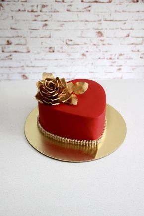 a red and gold heart shaped cake sitting on top of a white table next to a brick wall